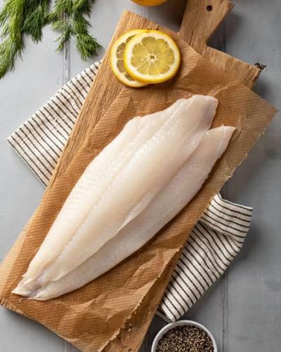 DRESSED SOLE Two raw fish fillets on a wooden cutting board with lemon slices and herbs.